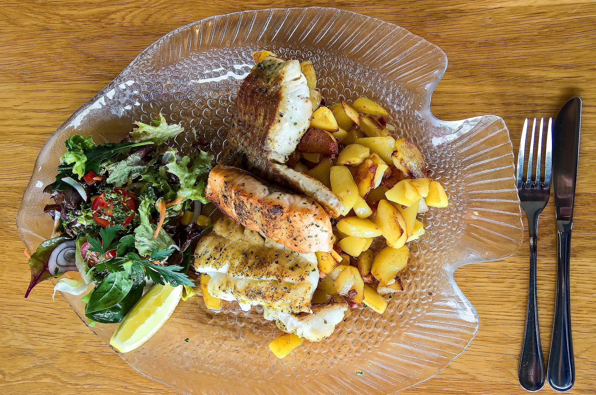salmon, salad and potatoes on a plate shaped like a fish