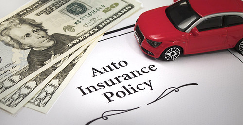 A red toy car and three 20 dollar bills on an auto insurance policy in Illinois.