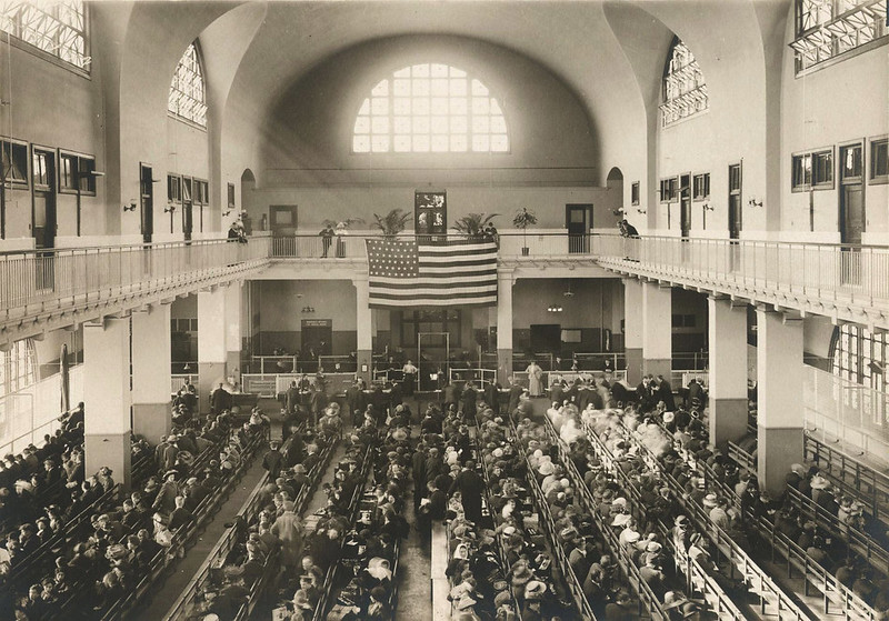 Older sepia photo of a large courtroom with an American flag hangs on the far wall
