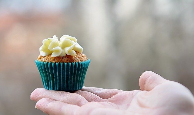 Mini cupcake with yellow icing being held in a hand