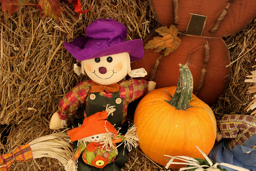 Small scarecrow doll sitting on hay with pumpkins